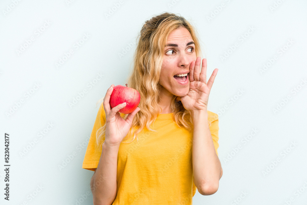 Young caucasian woman holding an apple isolated on blue background shouting and holding palm near opened mouth. Young caucasian woman holding an apple isolated on blue background shouting and holding palm near opened mouth.