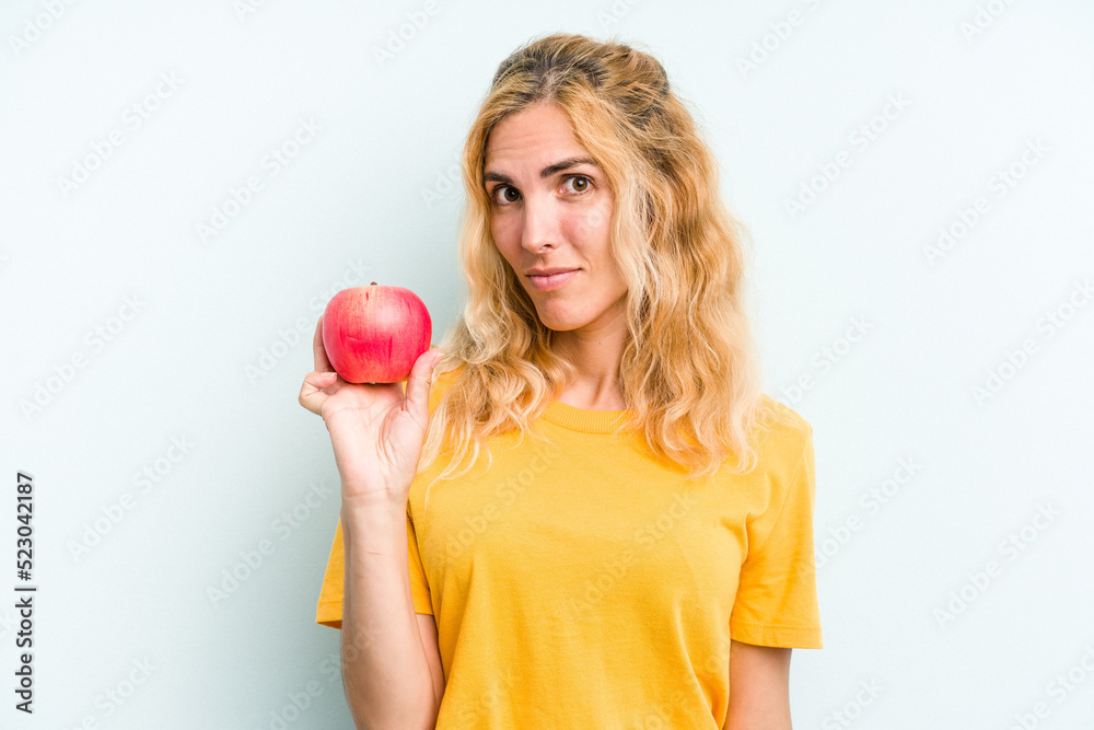 Young caucasian woman holding an apple isolated on blue background happy, smiling and cheerful. Young caucasian woman holding an apple isolated on blue background happy, smiling and cheerful.