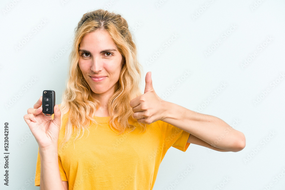 Young caucasian woman holding car keys isolated on blue background smiling and raising thumb up Young caucasian woman holding car keys isolated on blue background smiling and raising thumb up