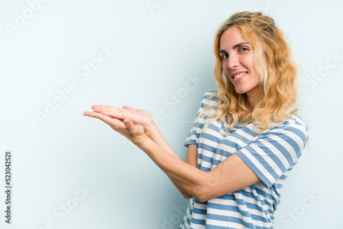 Young caucasian woman isolated on blue background holding a copy space on a palm.