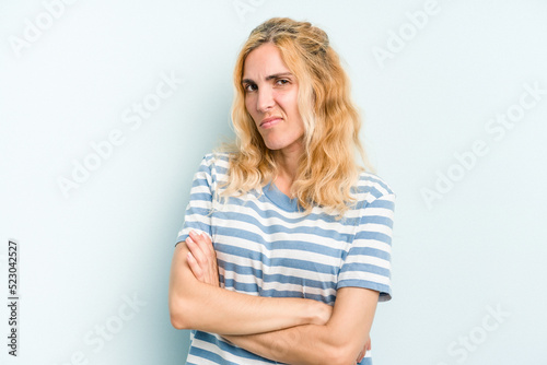 Young caucasian woman isolated on blue background frowning face in displeasure, keeps arms folded.