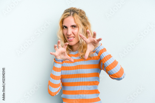 Young caucasian woman isolated on blue background showing claws imitating a cat, aggressive gesture.
