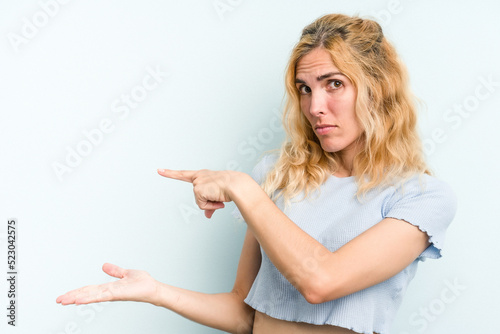 Young caucasian woman isolated on blue background excited holding a copy space on palm.