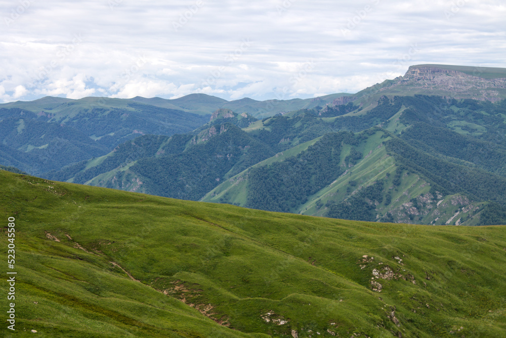 Panoramic view of green mountains and hills from the Bermamyt plateau in Karachay-Cherkessia in Russia on a cloudy summer day and a space for copying