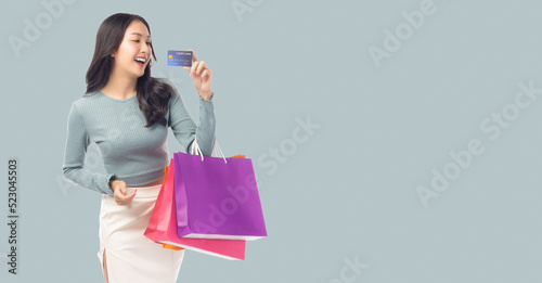 Young asian lady using credit card holding shopping bags isolated over pastel green background and copy space Smiling young girl shopping by using credit card Happy young woman look at credit card
