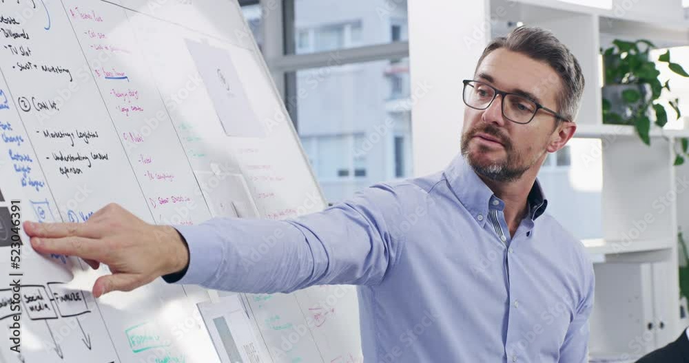 Confident business man leading a presentation in a meeting, pointing to and reading information on a board. Professional worker showing mission or vision plan and strategy during conference or speech