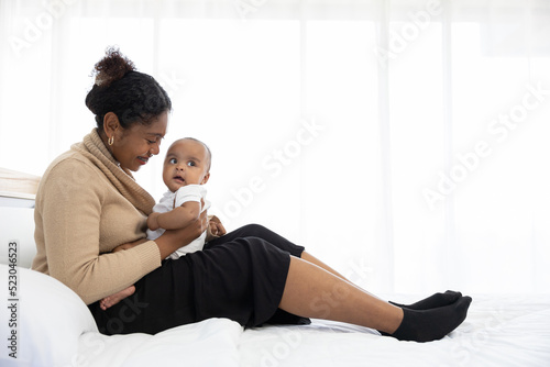 African young mother hugging and playing with her adorable baby on bed