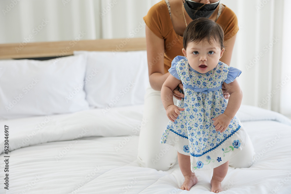 baby girl learning to walk and mother or sitter support her on bedroom baby girl learning to walk and mother or sitter support her on bedroom
