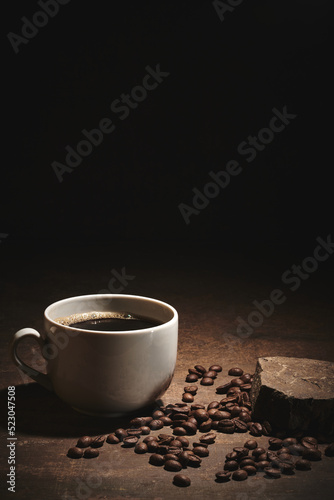 Cup of freshly brewed roasted coffee beans on brown background