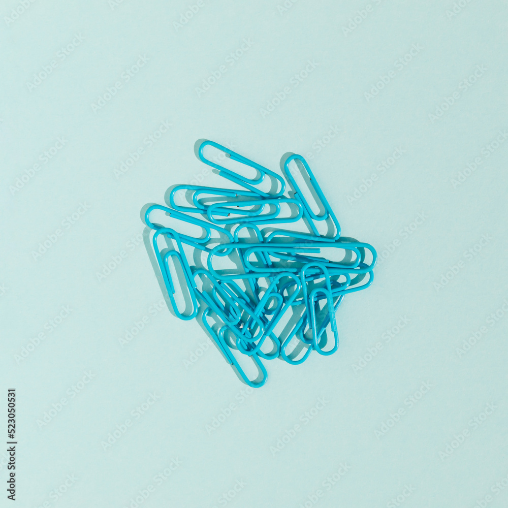 Paper clips isolated on blue background. Monochromatic composition. School or business concept. Flat lay, top view.