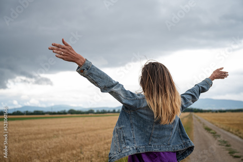 Young caucasian woman in jeans jacket celebrating life standing with her arms wide open