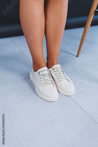 Women's legs close-up in white leather sneakers made from natural leather.Collection of women's summer shoes