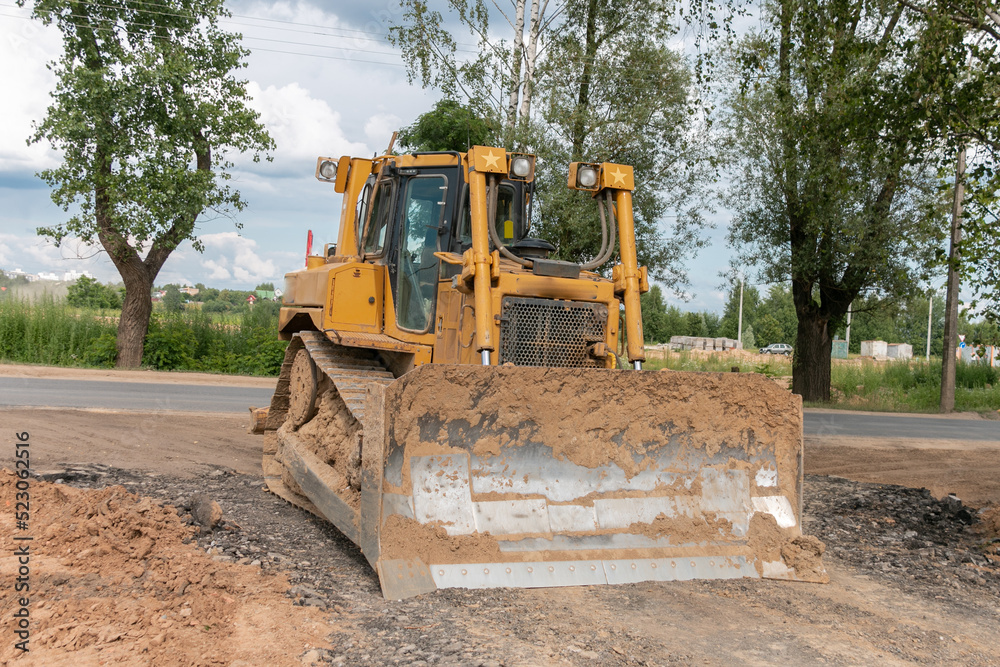 Obraz premium Crawler bulldozer clears the ground with a metal shield. Landscaping. Road construction works.