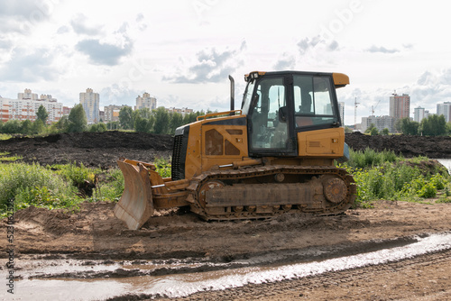 Crawler bulldozer clears the ground with a metal shield. Road construction works. The caterpillar bulldozer is used for layer-by-layer movement of soils.