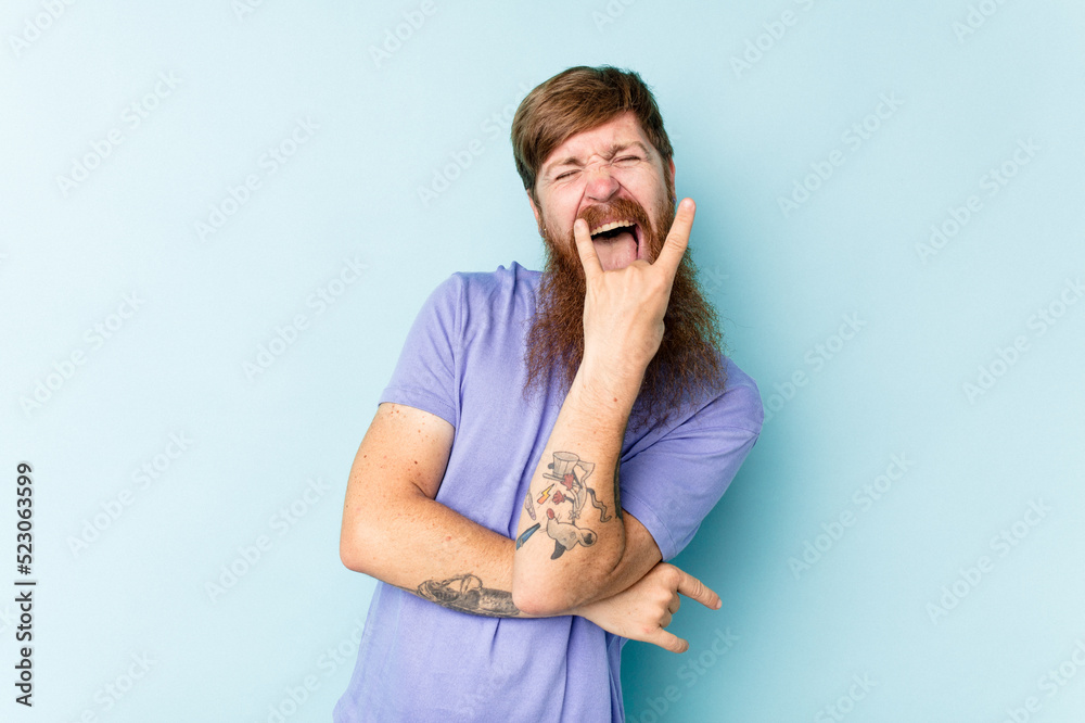 Young caucasian red-haired man isolated on blue background showing rock gesture with fingers Young caucasian red-haired man isolated on blue background showing rock gesture with fingers