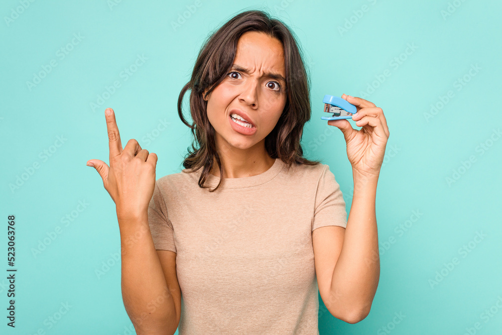 Young hispanic woman holding stapler isolated on blue background showing a disappointment gesture with forefinger. Young hispanic woman holding stapler isolated on blue background showing a disappointment gesture with forefinger.