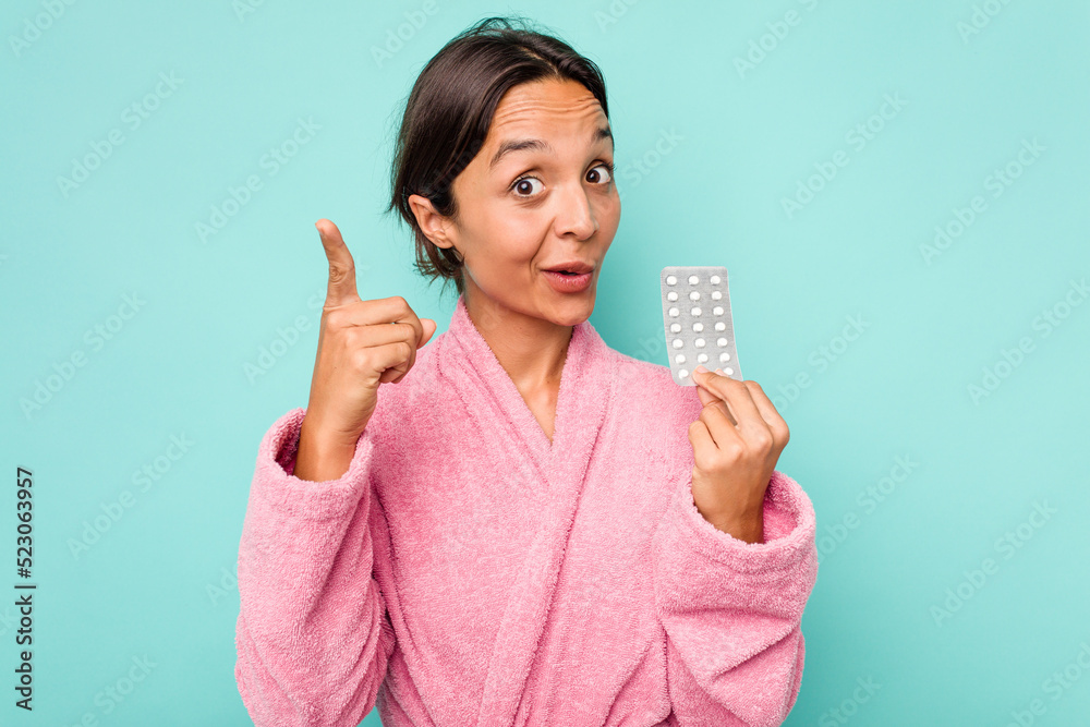 Young hispanic woman holding pills isolated on blue background having an idea, inspiration concept. Young hispanic woman holding pills isolated on blue background having an idea, inspiration concept.