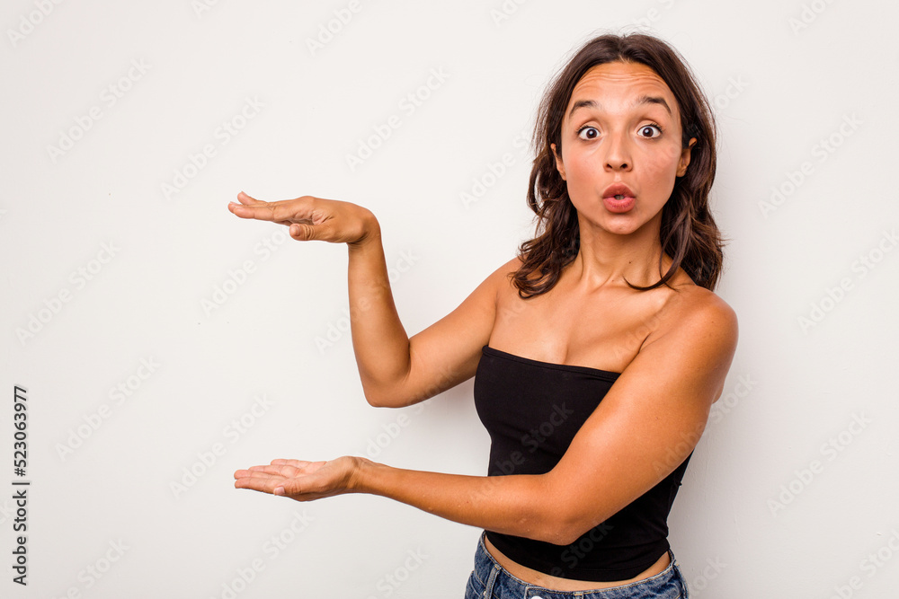 Young hispanic woman isolated on white background shocked and amazed holding a copy space between hands.