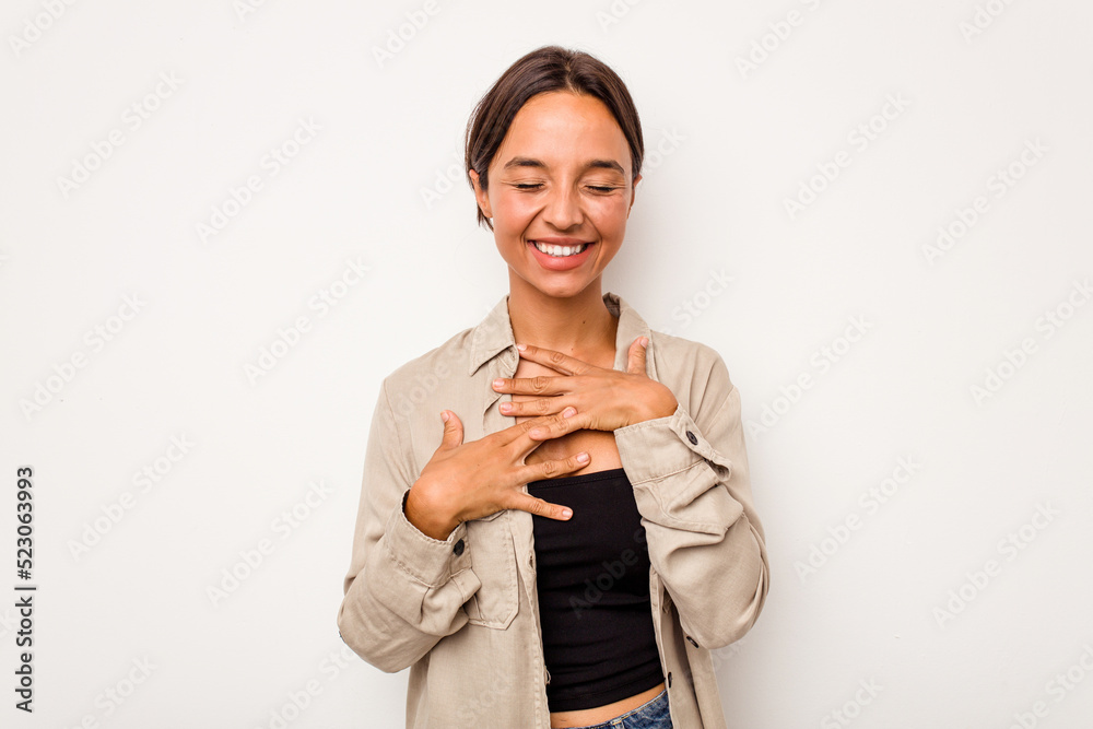 Young hispanic woman isolated on white background laughs happily and has fun keeping hands on stomach.