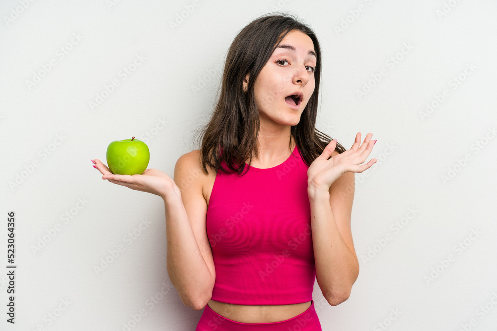Young caucasian woman holding an apple isolated on white background surprised and shocked. Young caucasian woman holding an apple isolated on white background surprised and shocked.