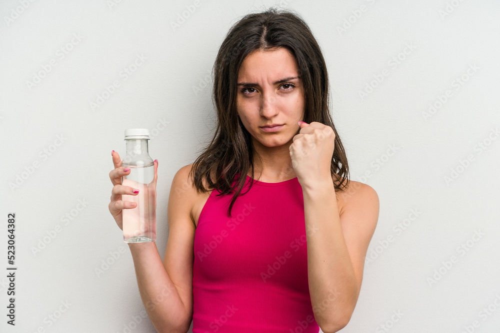 Young caucasian woman holding a bottle of water isolated on white background showing fist to camera, aggressive facial expression. Young caucasian woman holding a bottle of water isolated on white background showing fist to camera, aggressive facial expression.