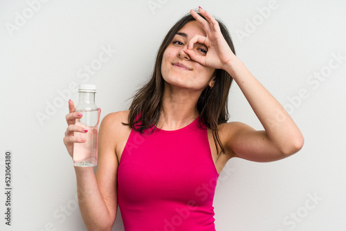 Young caucasian woman holding a bottle of water isolated on white background excited keeping ok gesture on eye.