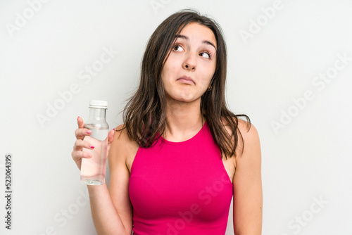 Young caucasian woman holding a bottle of water isolated on white background shrugs shoulders and open eyes confused. © Asier