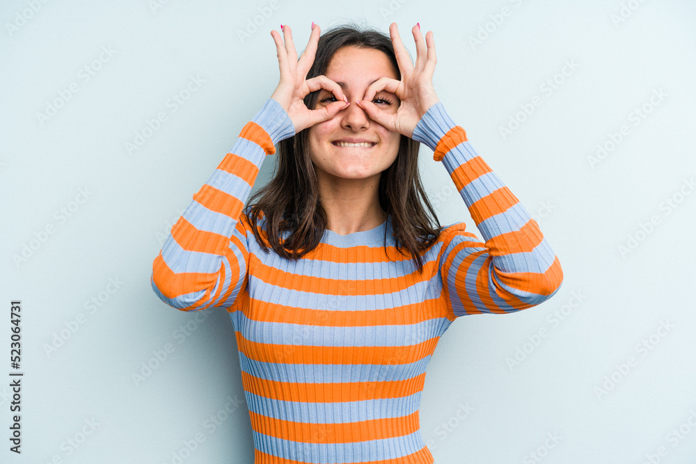 Young caucasian woman isolated on blue background showing okay sign over eyes Young caucasian woman isolated on blue background showing okay sign over eyes