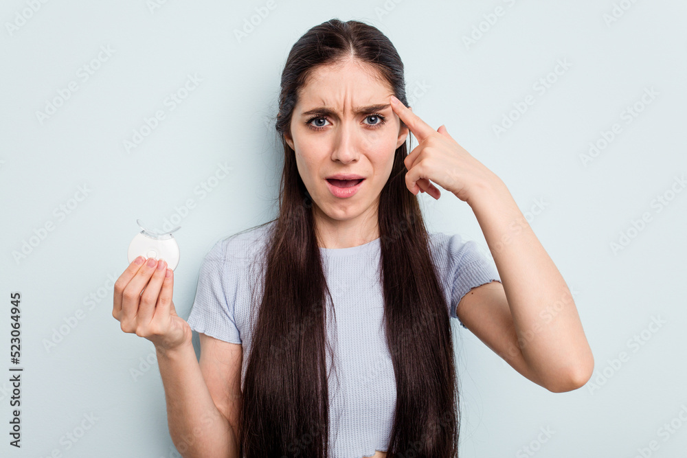 Young caucasian woman holding teeth whitener isolated on blue background showing a disappointment gesture with forefinger. Young caucasian woman holding teeth whitener isolated on blue background showing a disappointment gesture with forefinger.