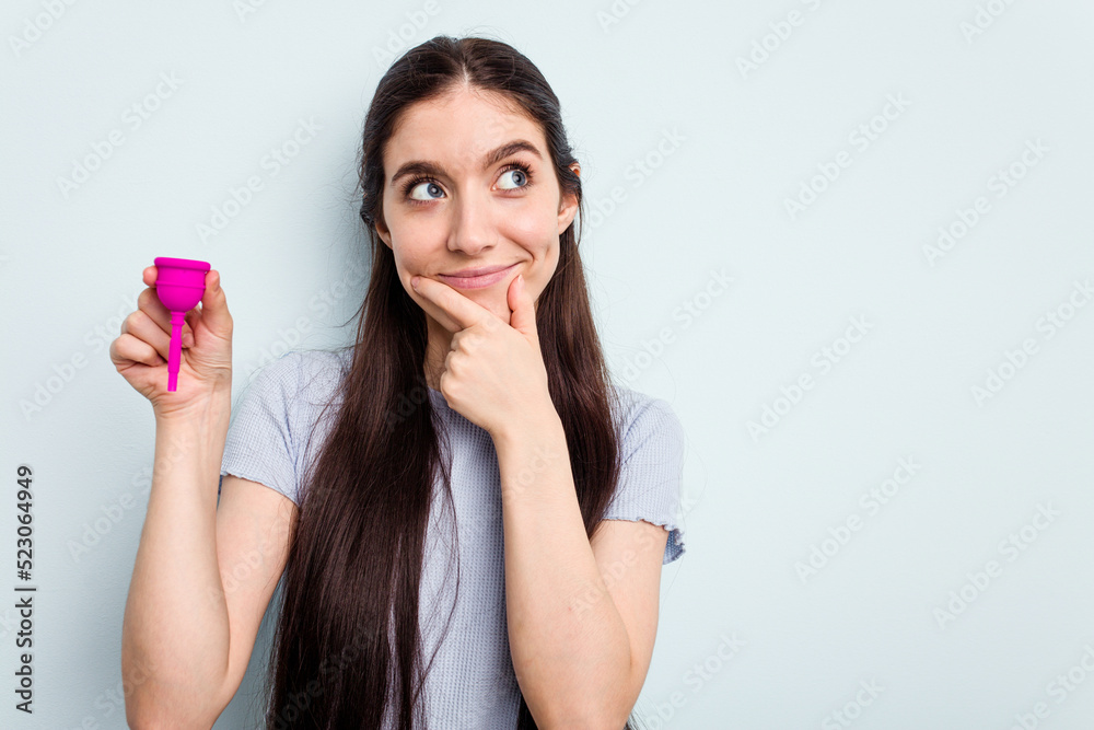 Young caucasian woman holding a sanitary napkin isolated on blue background looking sideways with doubtful and skeptical expression. Young caucasian woman holding a sanitary napkin isolated on blue background looking sideways with doubtful and skeptical expression.