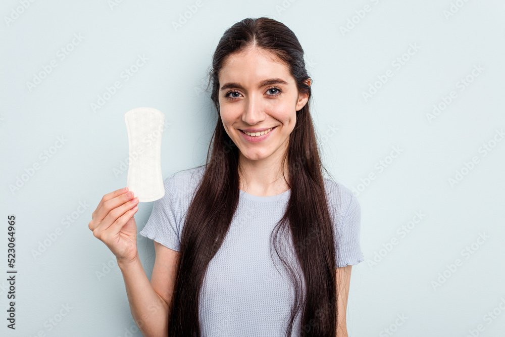 Young caucasian woman holding a sanitary napkin isolated on blue background happy, smiling and cheerful. Young caucasian woman holding a sanitary napkin isolated on blue background happy, smiling and cheerful.