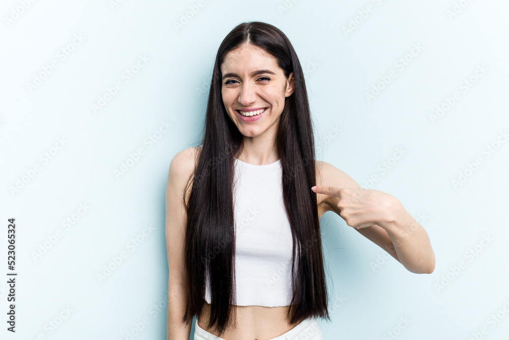 Young caucasian woman isolated on blue background person pointing by hand to a shirt copy space, proud and confident