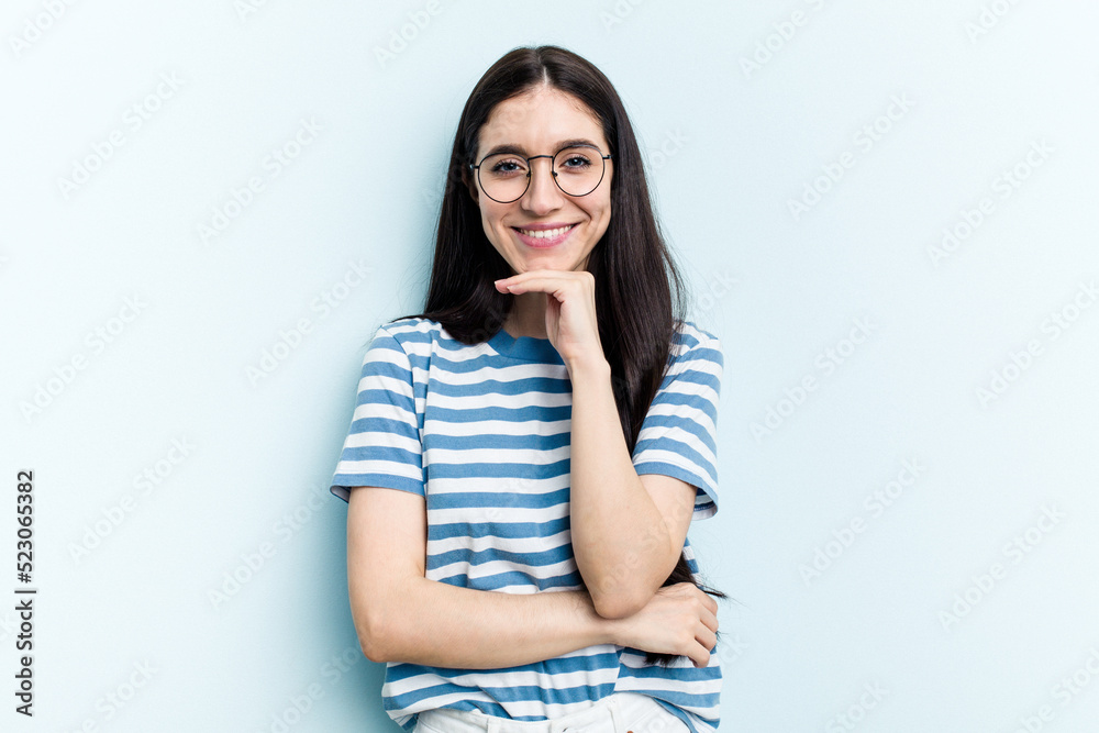 Young caucasian woman isolated on blue background smiling happy and confident, touching chin with hand. Young caucasian woman isolated on blue background smiling happy and confident, touching chin with hand.