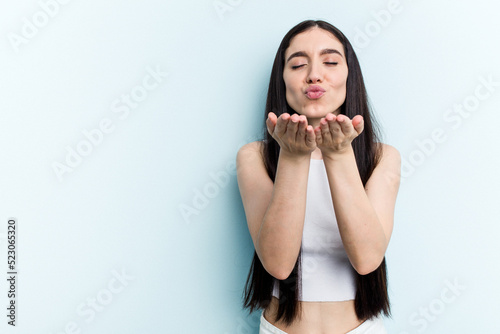 Young caucasian woman isolated on blue background folding lips and holding palms to send air kiss.