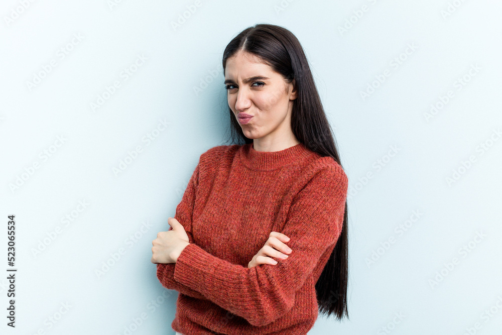 Young caucasian woman isolated on blue background frowning face in displeasure, keeps arms folded. Young caucasian woman isolated on blue background frowning face in displeasure, keeps arms folded.