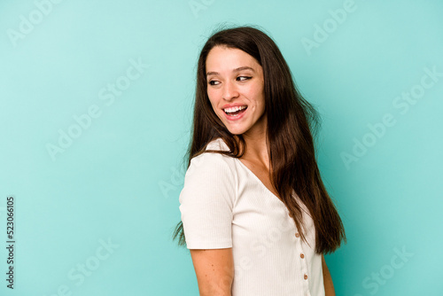 Young caucasian woman isolated on blue background looks aside smiling, cheerful and pleasant.