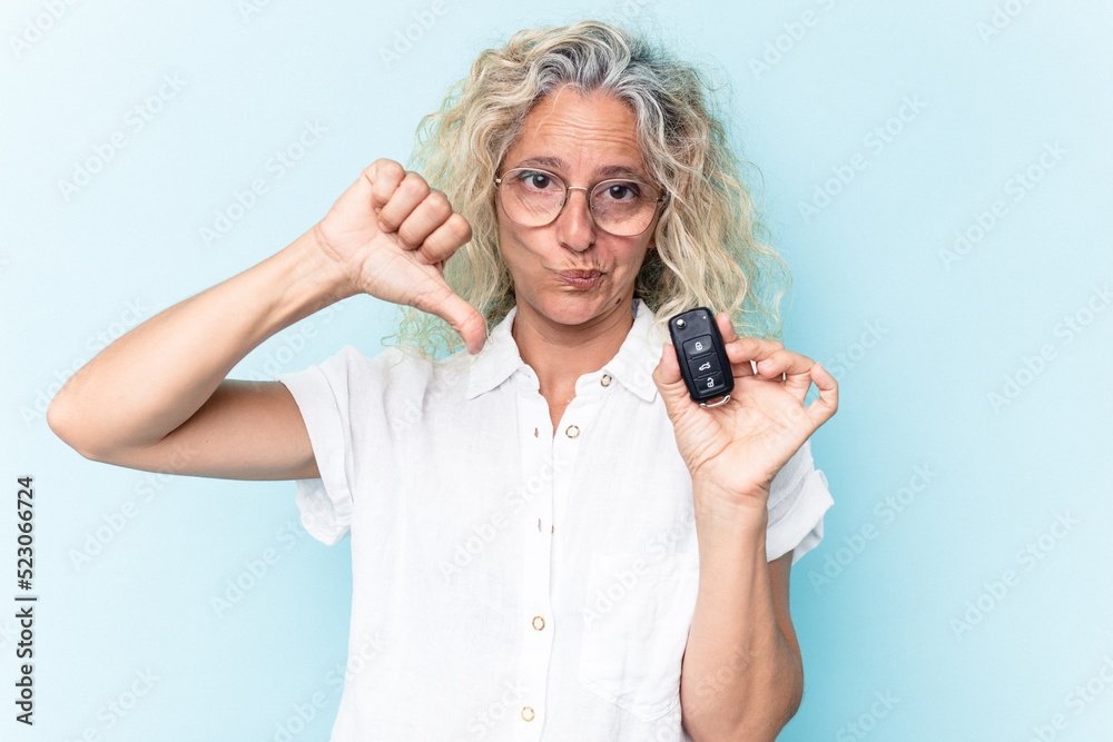 Middle age caucasian woman holding a car keys isolated on blue background showing a dislike gesture, thumbs down. Disagreement concept.