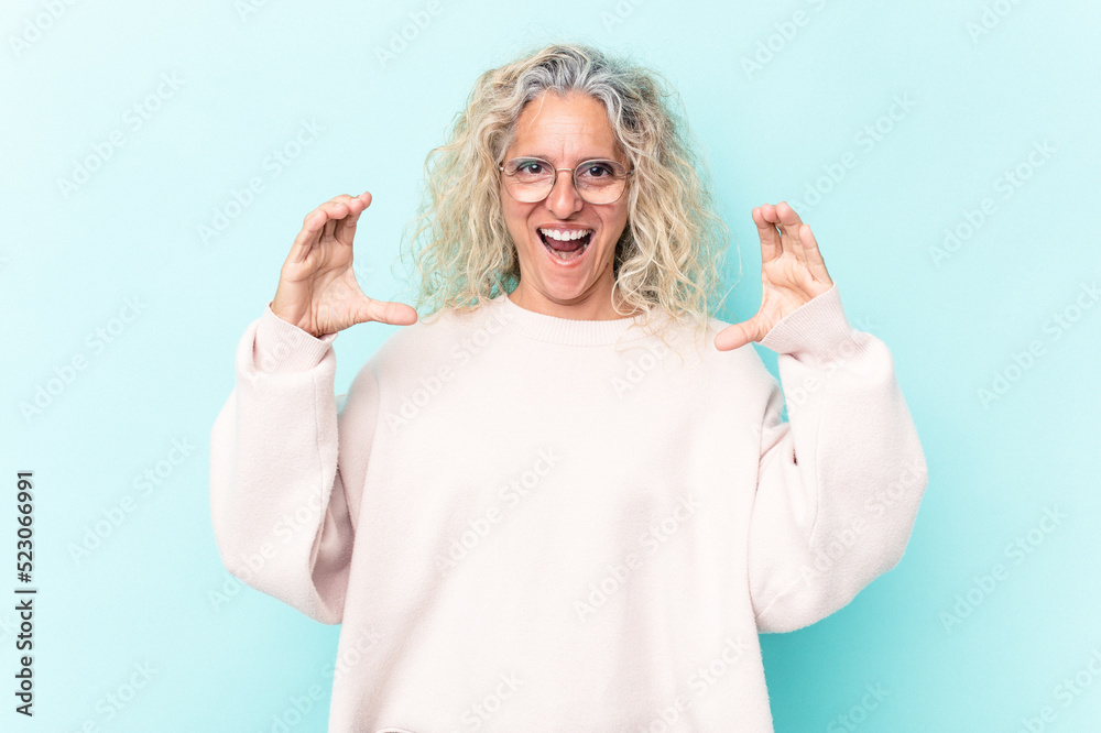 Middle age caucasian woman isolated on blue background holding something with palms, offering to camera. Middle age caucasian woman isolated on blue background holding something with palms, offering to camera.