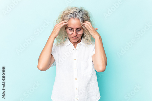 Middle age caucasian woman isolated on blue background touching temples and having headache.