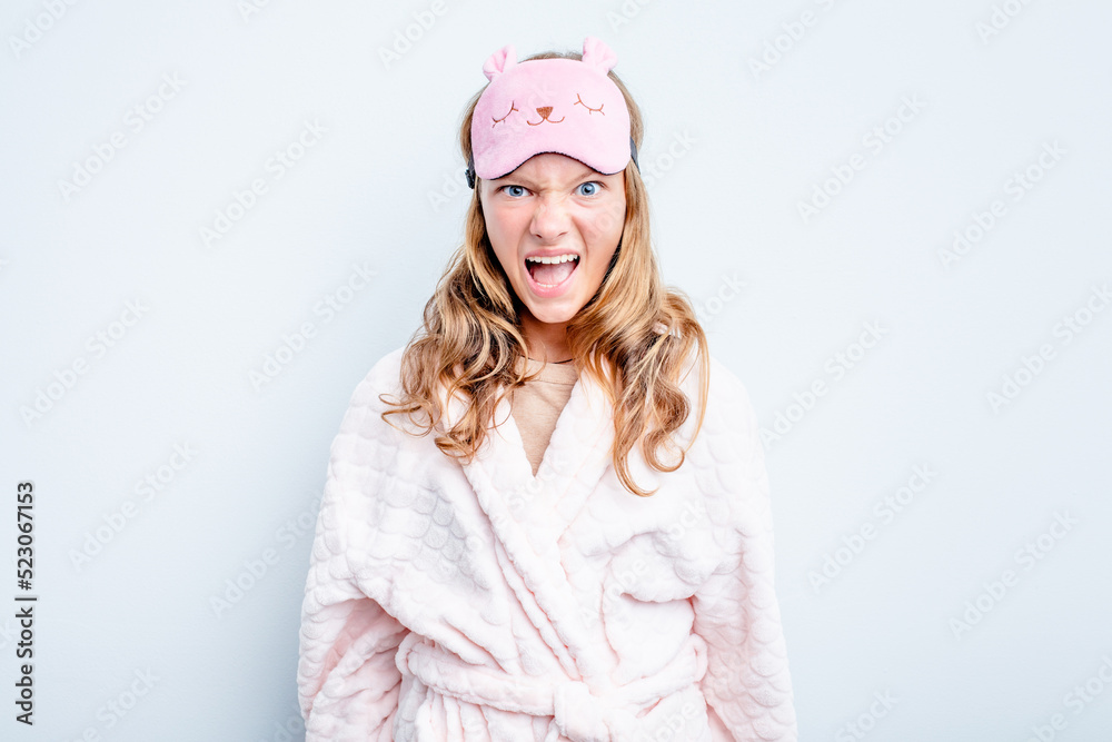 Caucasian teen girl wearing a pajama isolated on blue background screaming very angry and aggressive. Caucasian teen girl wearing a pajama isolated on blue background screaming very angry and aggressive.