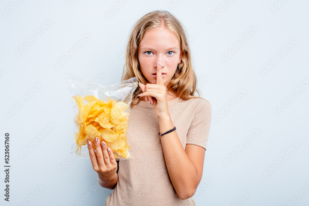 Caucasian teen girl holding bag of chips isolated on blue background keeping a secret or asking for silence. Caucasian teen girl holding bag of chips isolated on blue background keeping a secret or asking for silence.