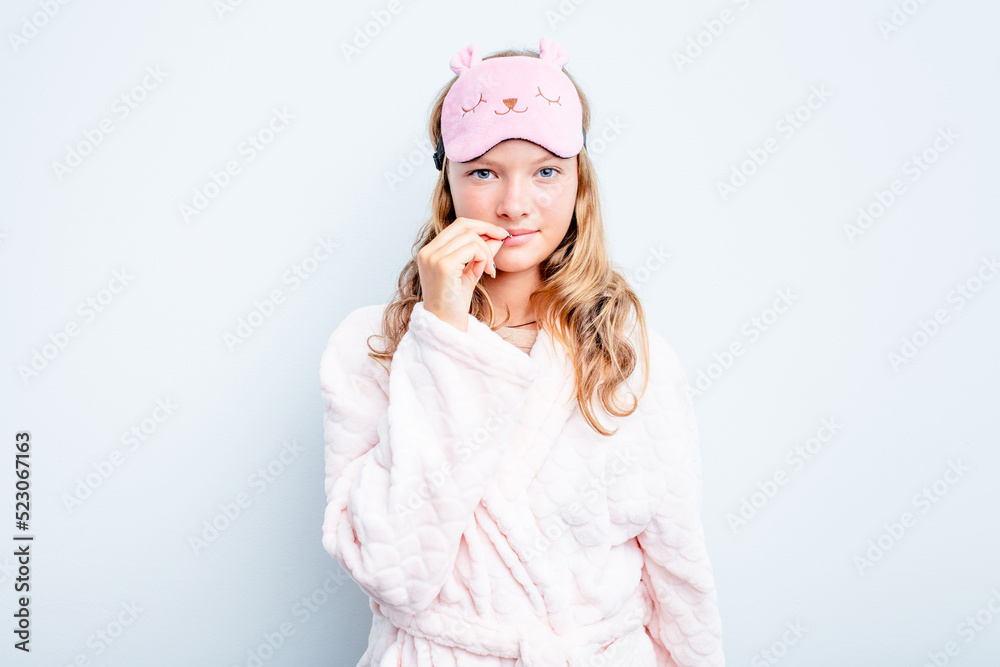 Caucasian teen girl wearing a pajama isolated on blue background with fingers on lips keeping a secret. Caucasian teen girl wearing a pajama isolated on blue background with fingers on lips keeping a secret.