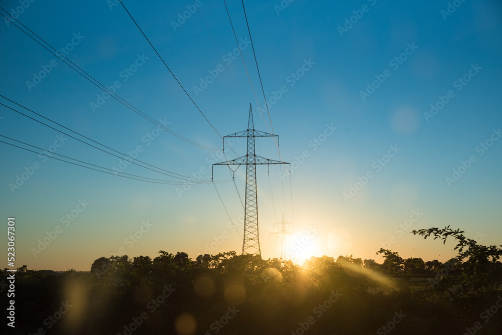 Fototapeta premium high-voltage line over at sunset, tree alley silouette