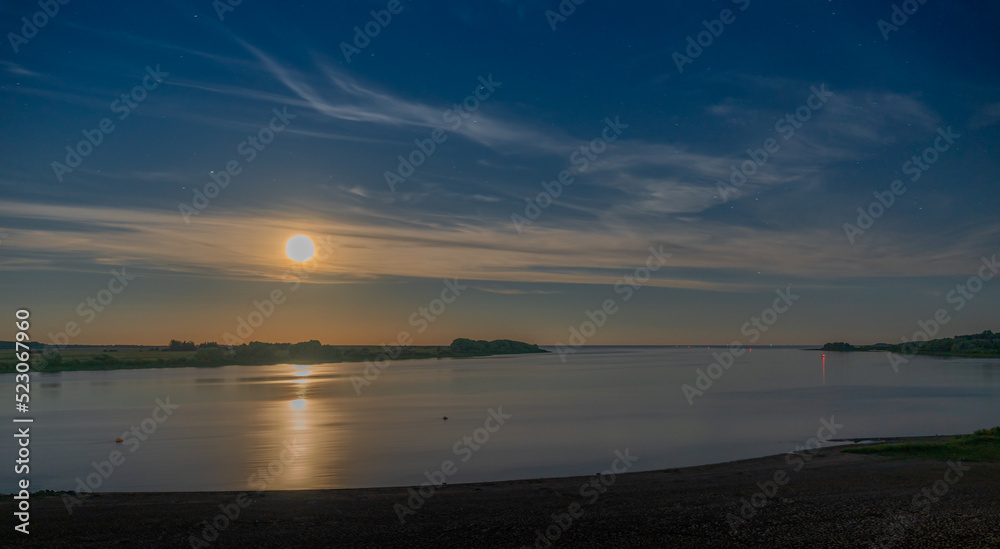Moonrise over the river in the starry sky in light clouds. Night landscape