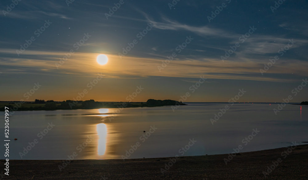 Moonrise over the river in the starry sky in light clouds. Night landscape