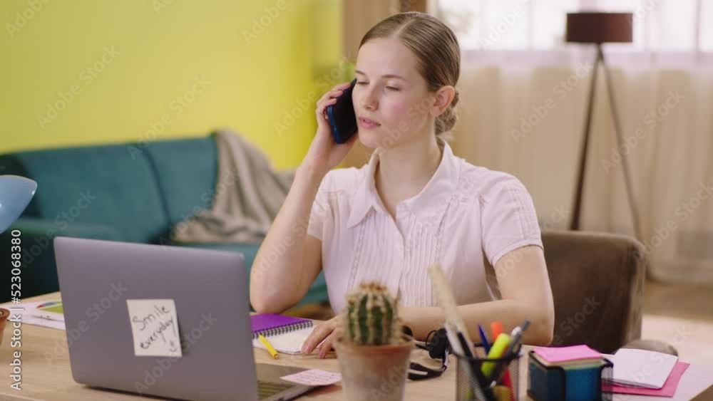 Call centre agent working from home at her laptop she make a call with a client she using the smartphone Call centre agent working from home at her laptop she make a call with a client she using the smartphone