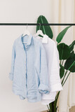 Two shirts hang on hangers. Natural. White and blue linen long sleeve shirts. Summer clothes