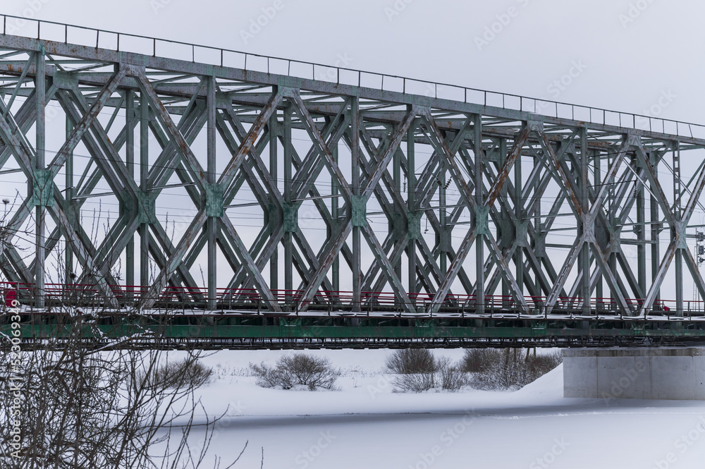 Naklejka premium Old railway bridge across the river in winter. Footprints under the bridge