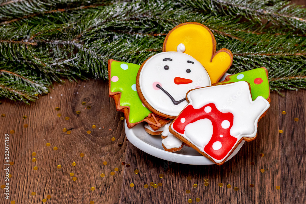 Christmas cookies in a plate on a table near a snowy fir tree branch