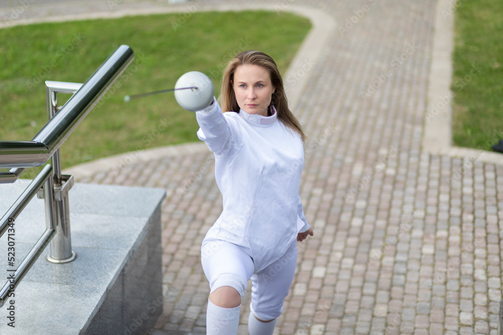 Woman in white fencing costume stays on stairs outdoor in attacking
